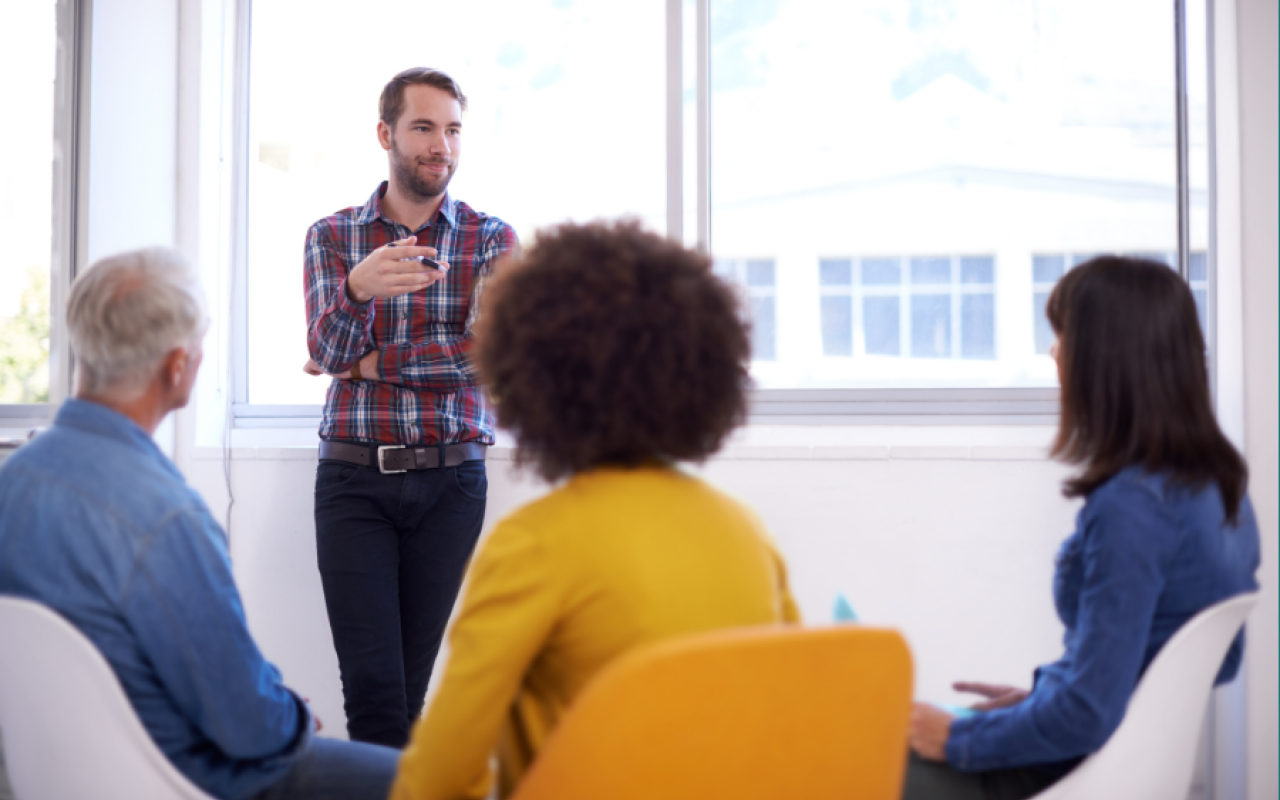 A man is standing up and talking to three people who are sitting down